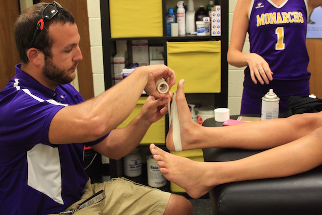 Athletic trainer Jonathan Hornsby bandages an injured athlete 