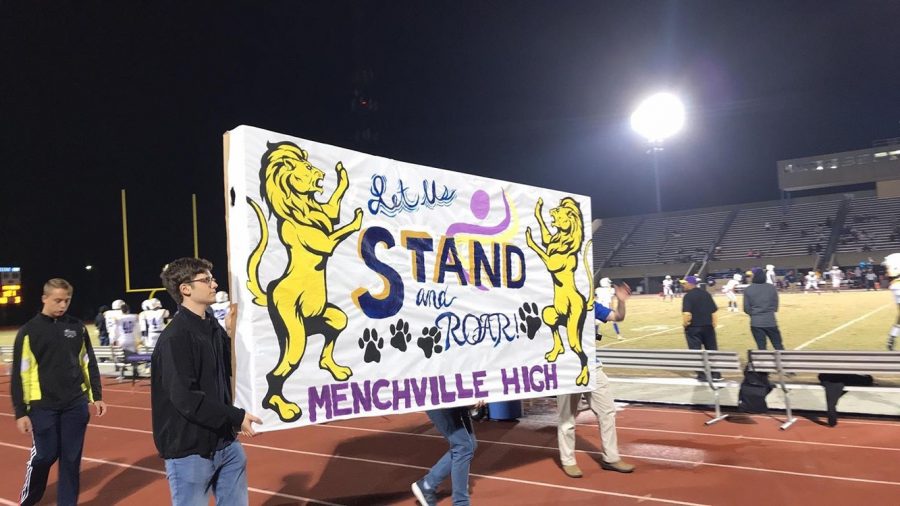 Menchville students march around the track with their banner at half-time of the football game.