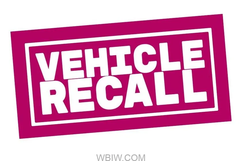 Rows of recalled cars and trucks under a safety warning banner